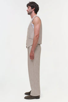 Man wearing beige sleeveless vest and matching trousers in side profile view.