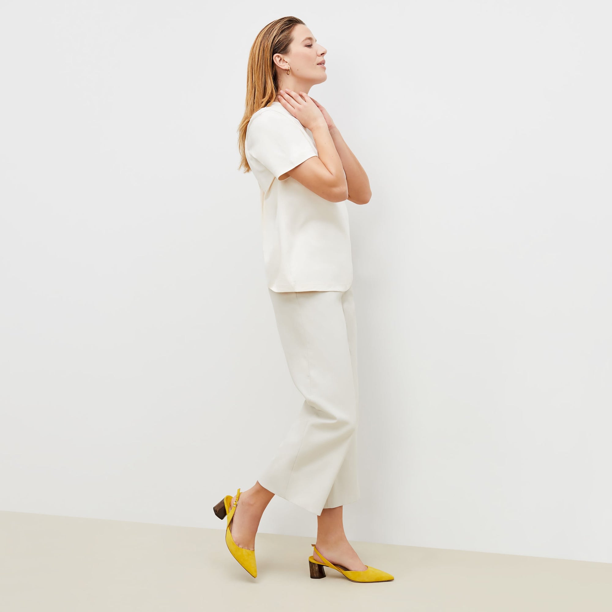 Side image of a woman standing wearing the leslie top in compact cotton in ivory | Exclude