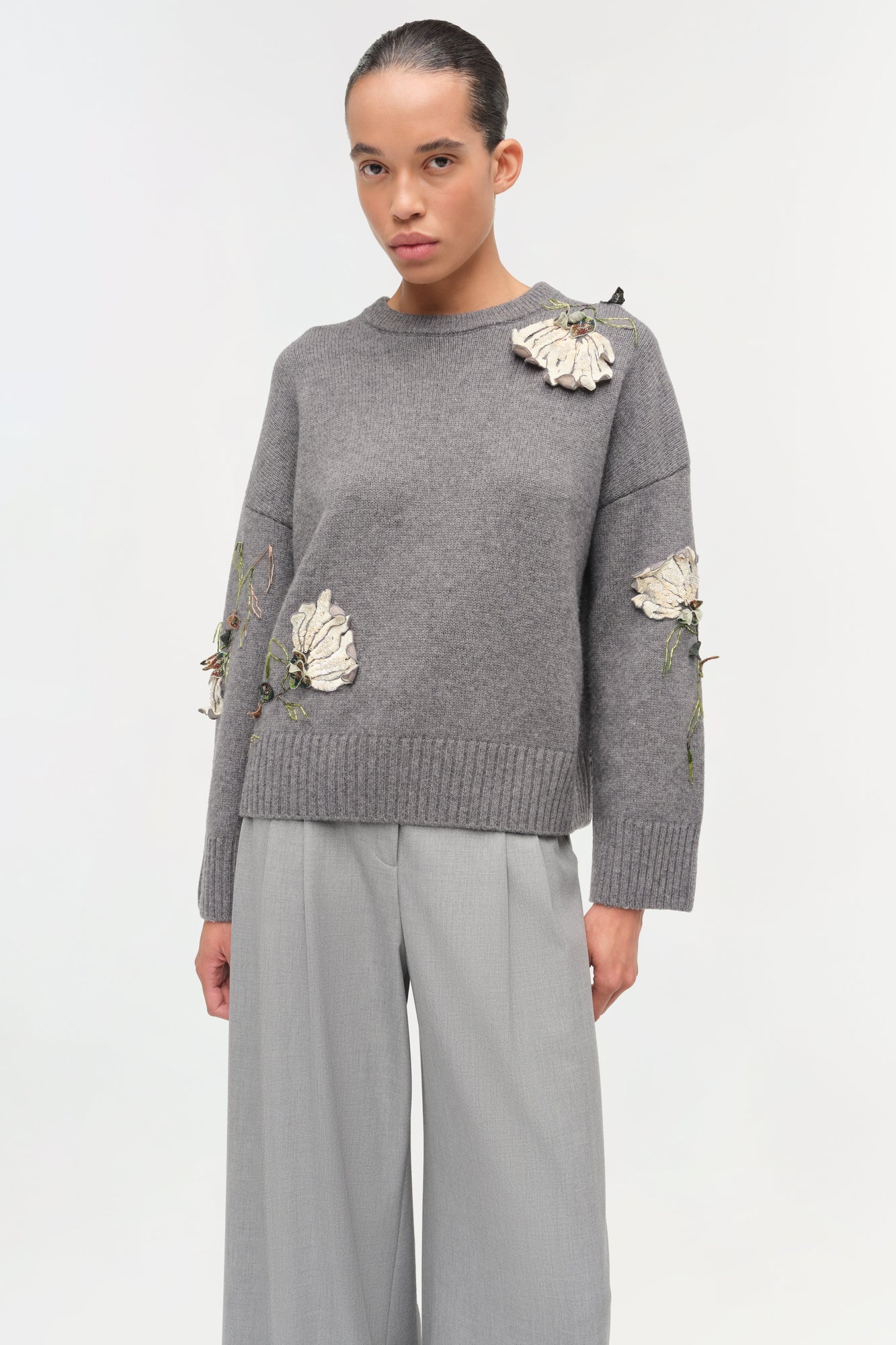 Gray crewneck sweater with cream floral embellishments and green embroidered details on shoulder and sleeves.