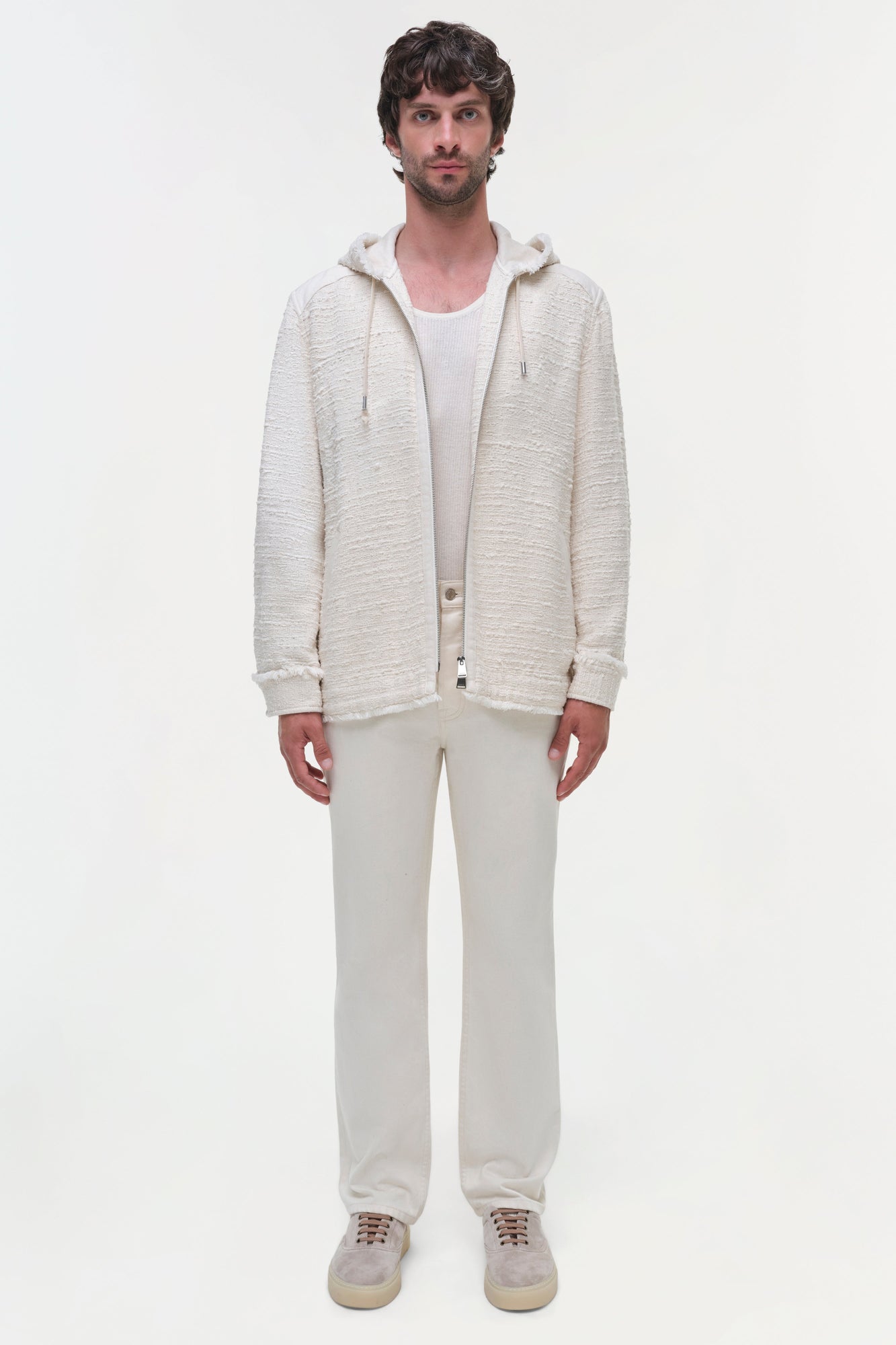 Man wearing cream hooded zip-up jacket over white ribbed shirt with cream pants and sneakers.