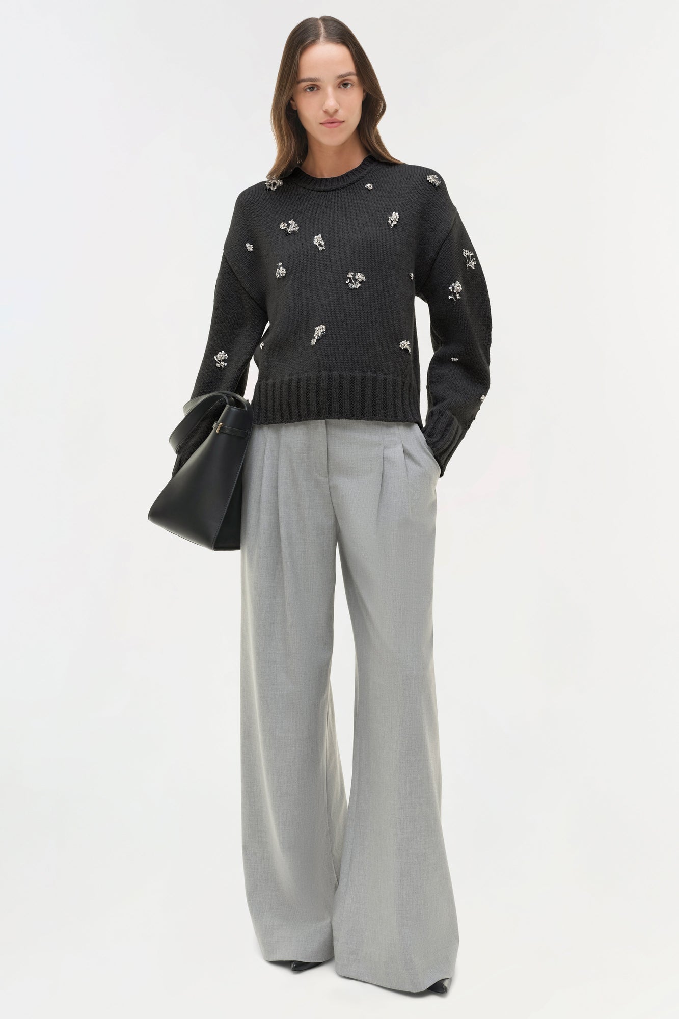 Black knit crewneck sweater with white floral embellishments, worn with gray wide-leg trousers.