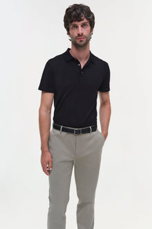 Man wearing beige cotton twill trousers with black polo shirt and belt.
