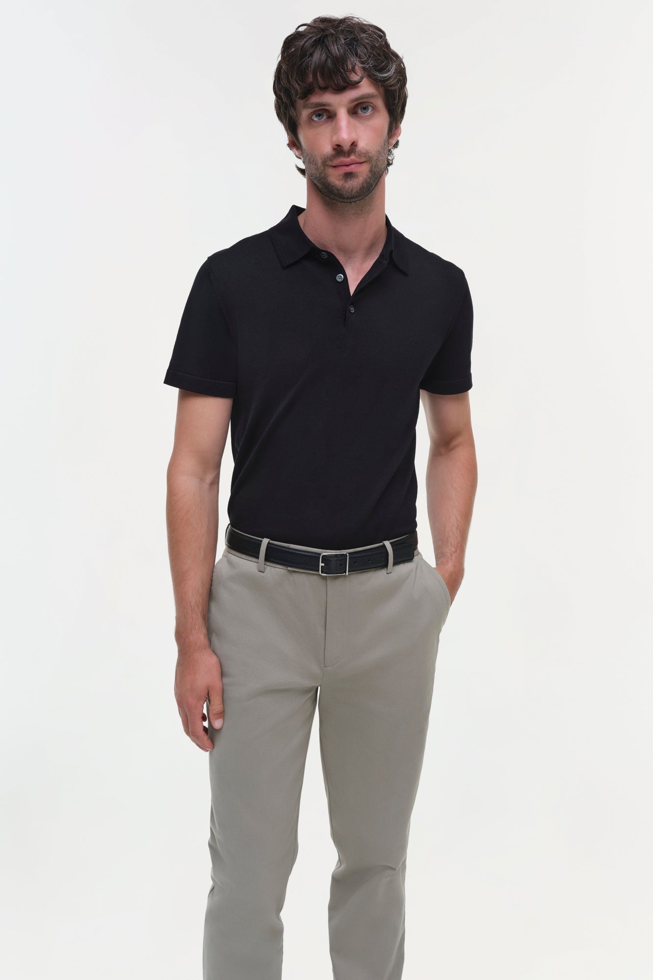 Man wearing beige cotton twill trousers with black polo shirt and belt.