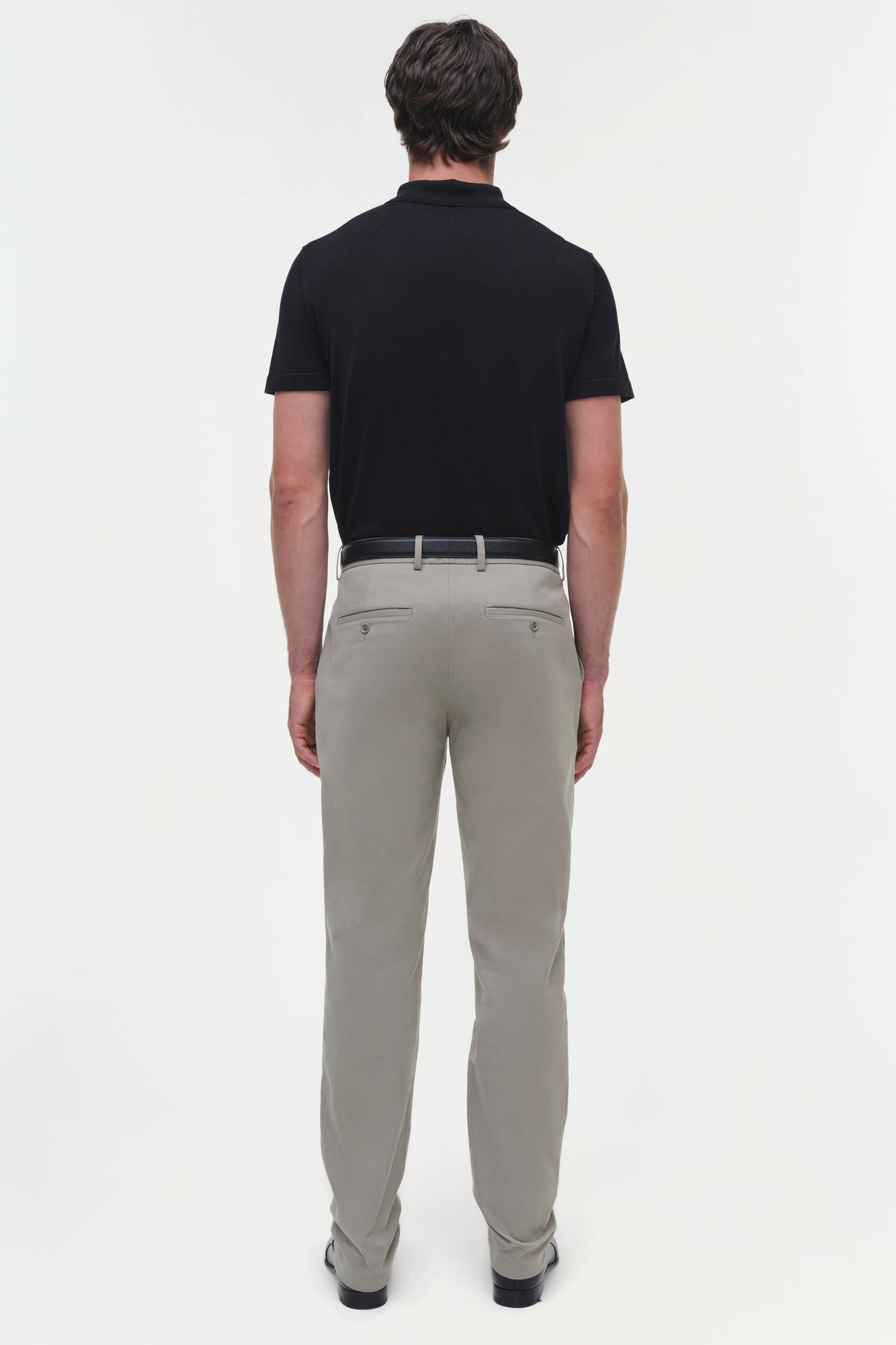 Man wearing black polo shirt and beige cotton twill trousers with belt, shown from back view.