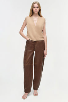 Brown leather pants with curved leg silhouette, worn with beige knit vest.
