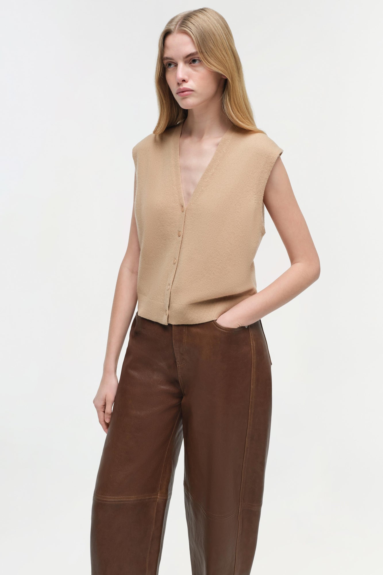 Beige sleeveless cashmere vest with button front and V-neckline worn over brown pants.