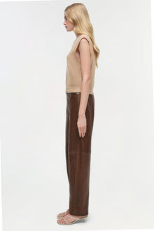 Brown leather pants with curved leg silhouette, shown on model wearing beige sleeveless top.