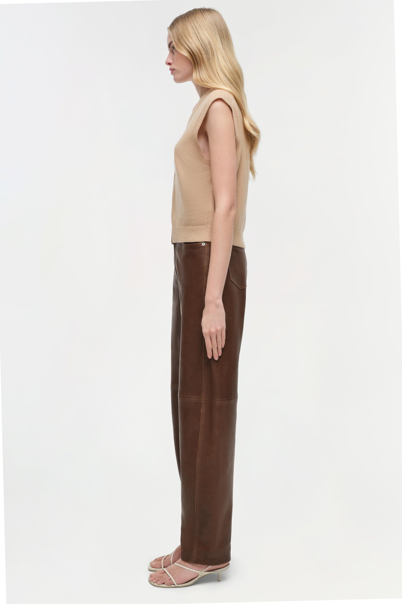 Brown leather pants with curved leg silhouette, shown on model wearing beige sleeveless top.