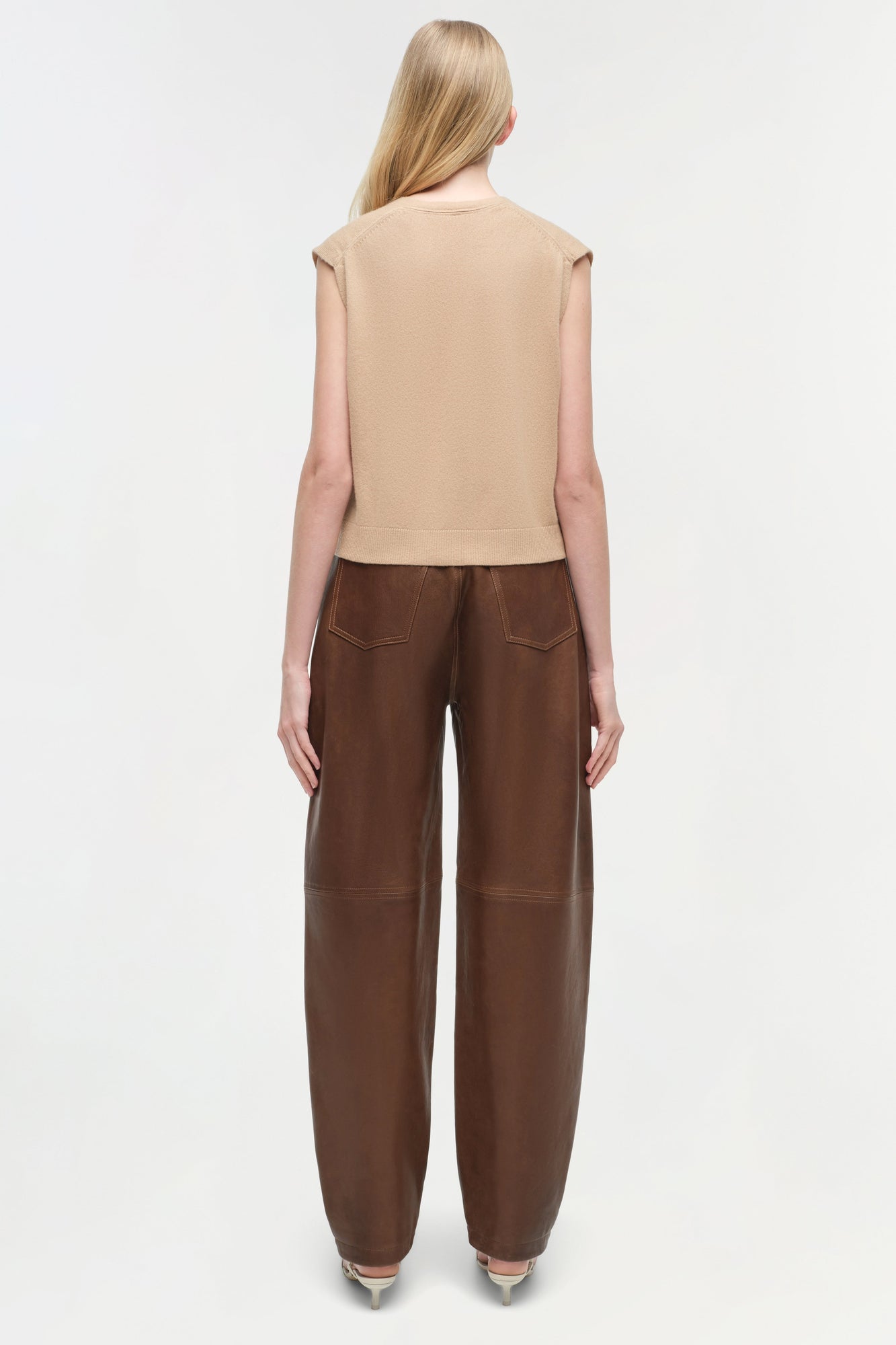 Brown leather pants with curved legs and visible topstitching, shown from back view on model.