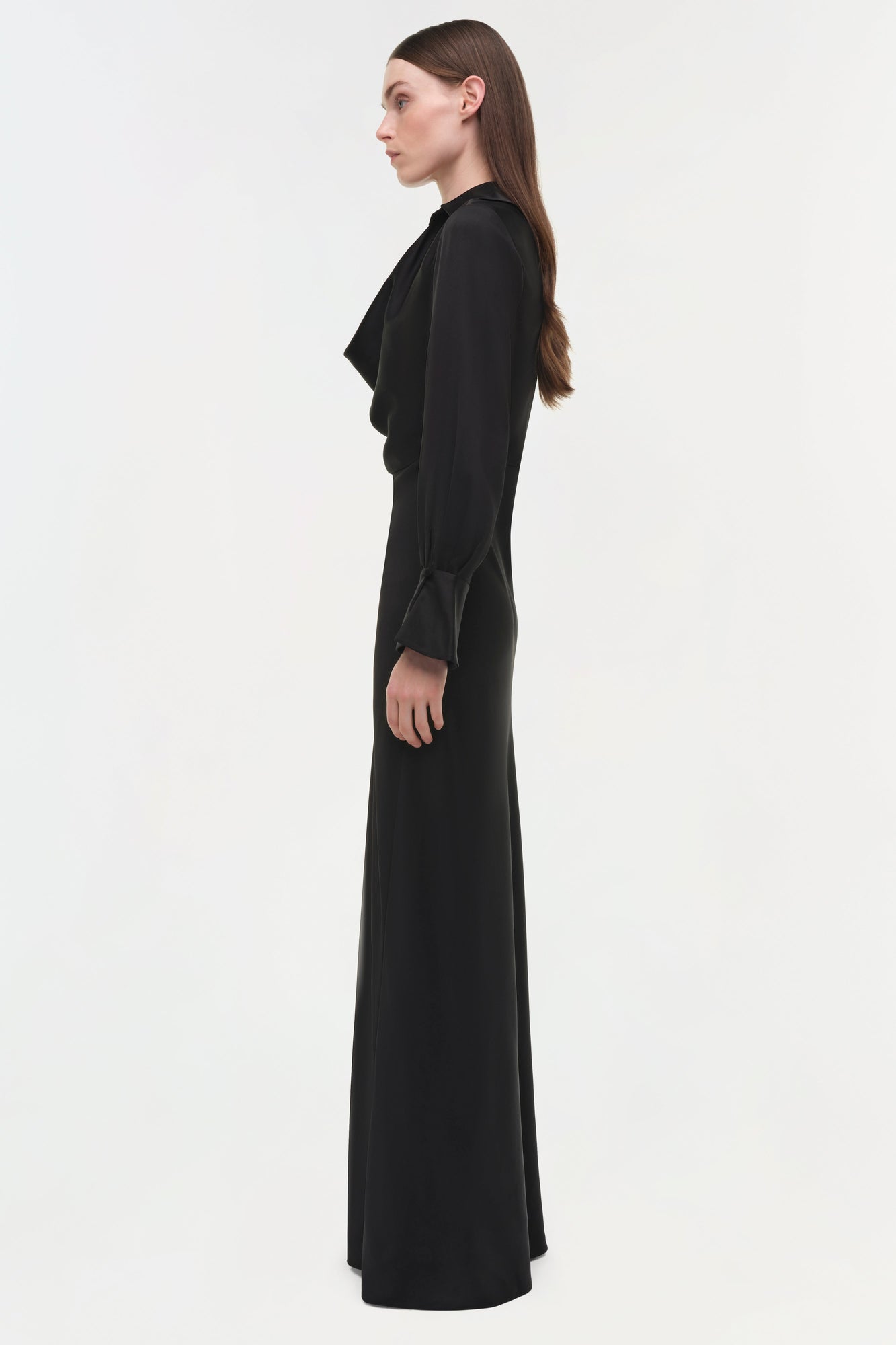 Black satin gown with draped side detail and long sleeves, shown on model in profile.