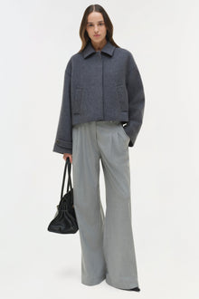 Charcoal wool jacket with pointed collar, front button closure, and patch pockets worn with gray trousers.