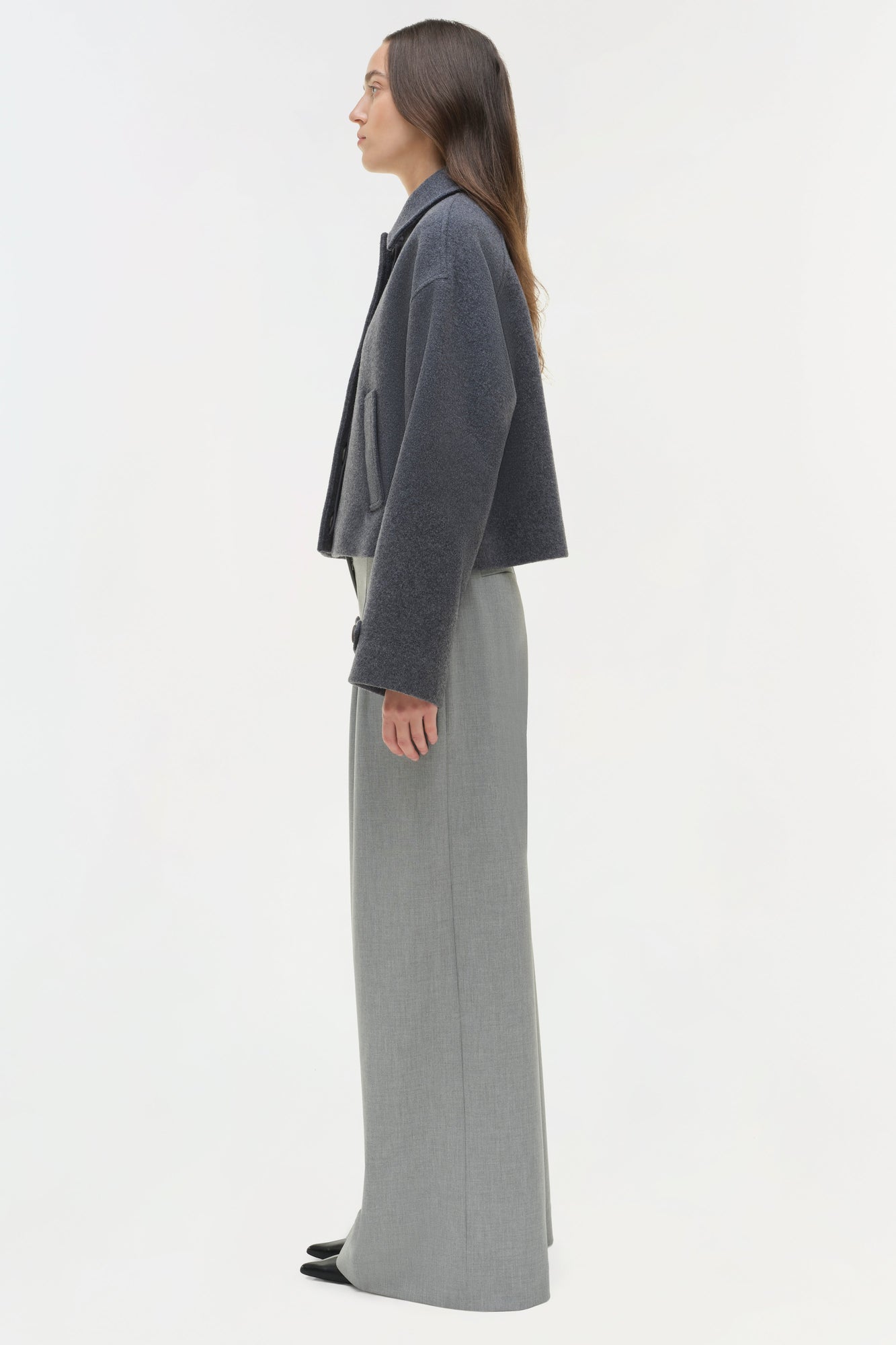 Woman wearing charcoal wool jacket with notch collar over light gray wide-leg trousers, shown in profile view.