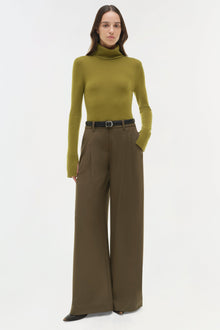 Woman wearing olive turtleneck with wide-leg brown trousers and black belt.