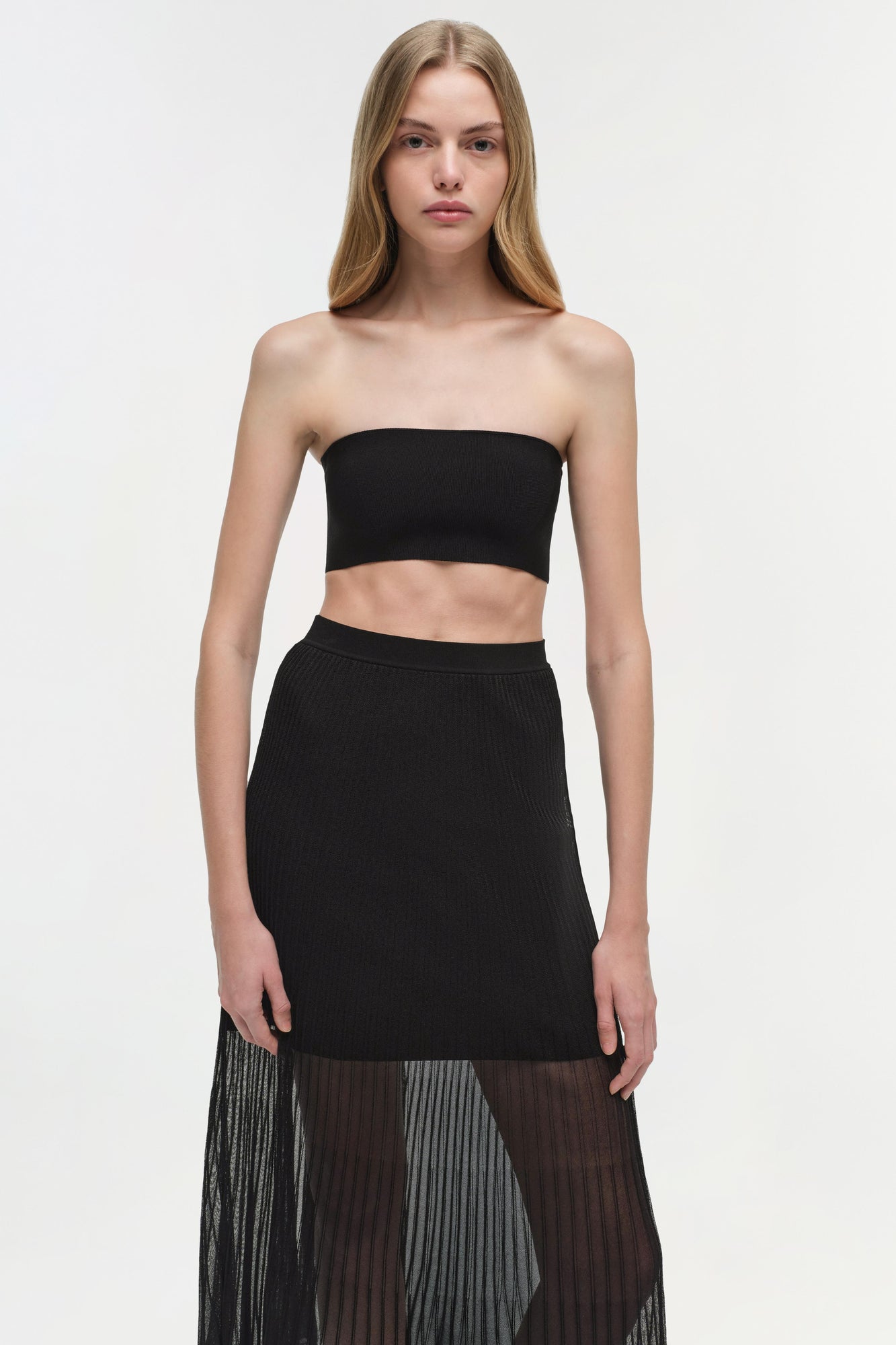 Black knit bralette with strapless, seamless design on model wearing black skirt.