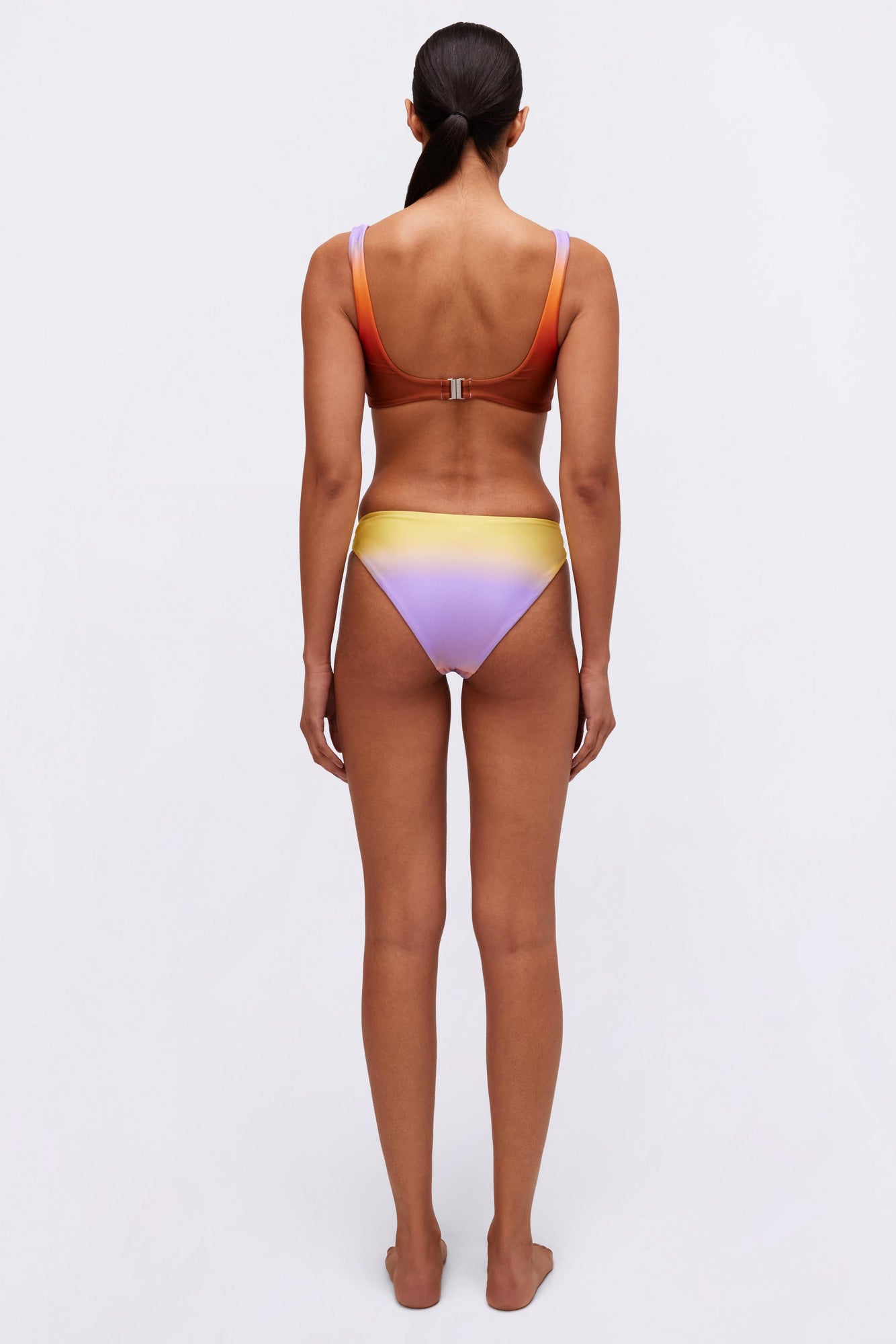 Woman wearing a two-piece swimsuit with a red and purple ombre bikini top and yellow-to-purple gradient bottom, viewed from b
