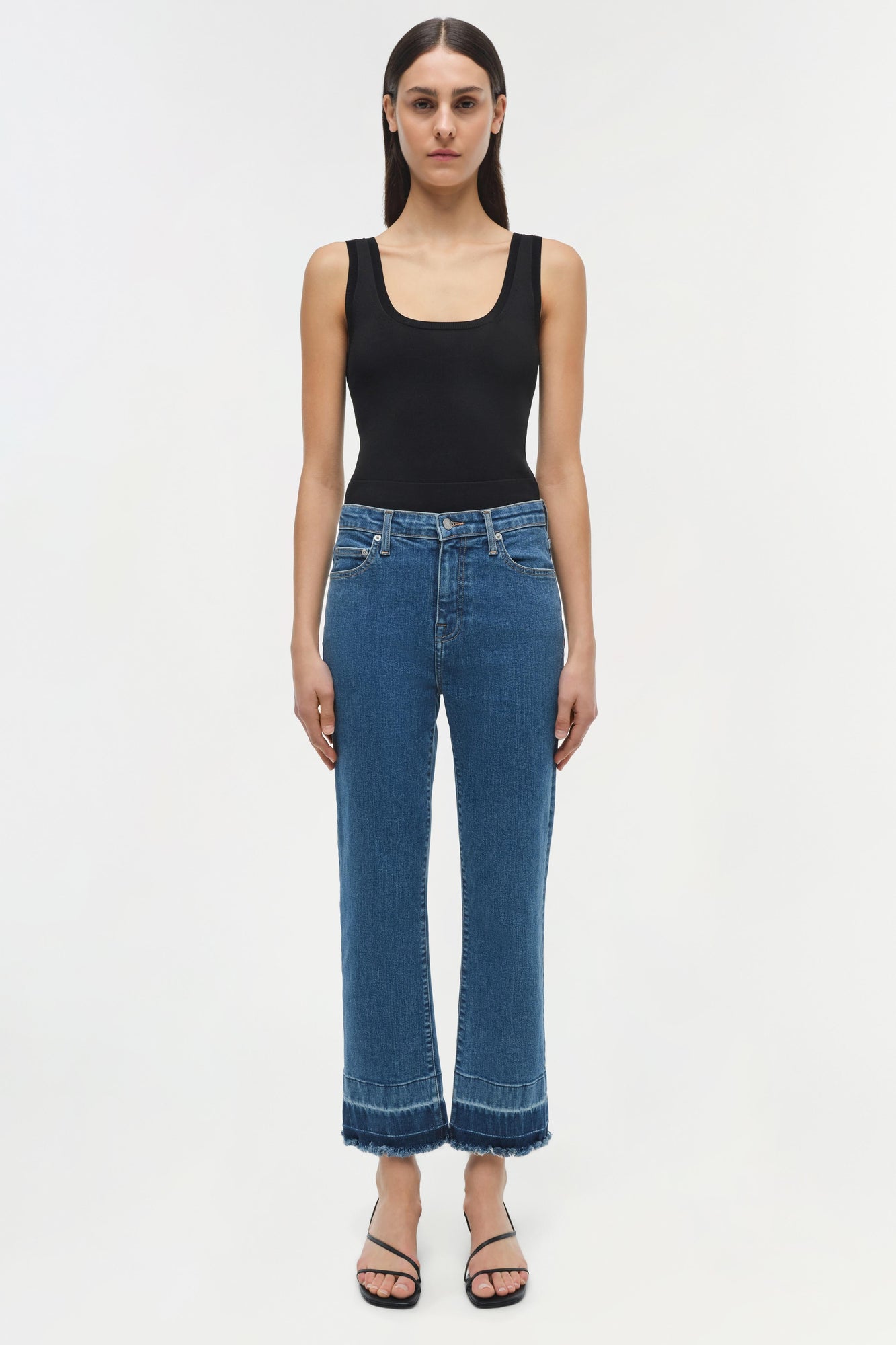 Woman wearing blue straight-leg jeans with frayed hem and black sleeveless tank top.