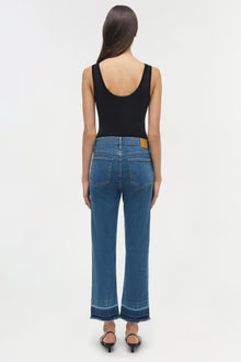 Woman wearing blue straight-leg jeans with frayed hems and a black sleeveless top, viewed from behind.