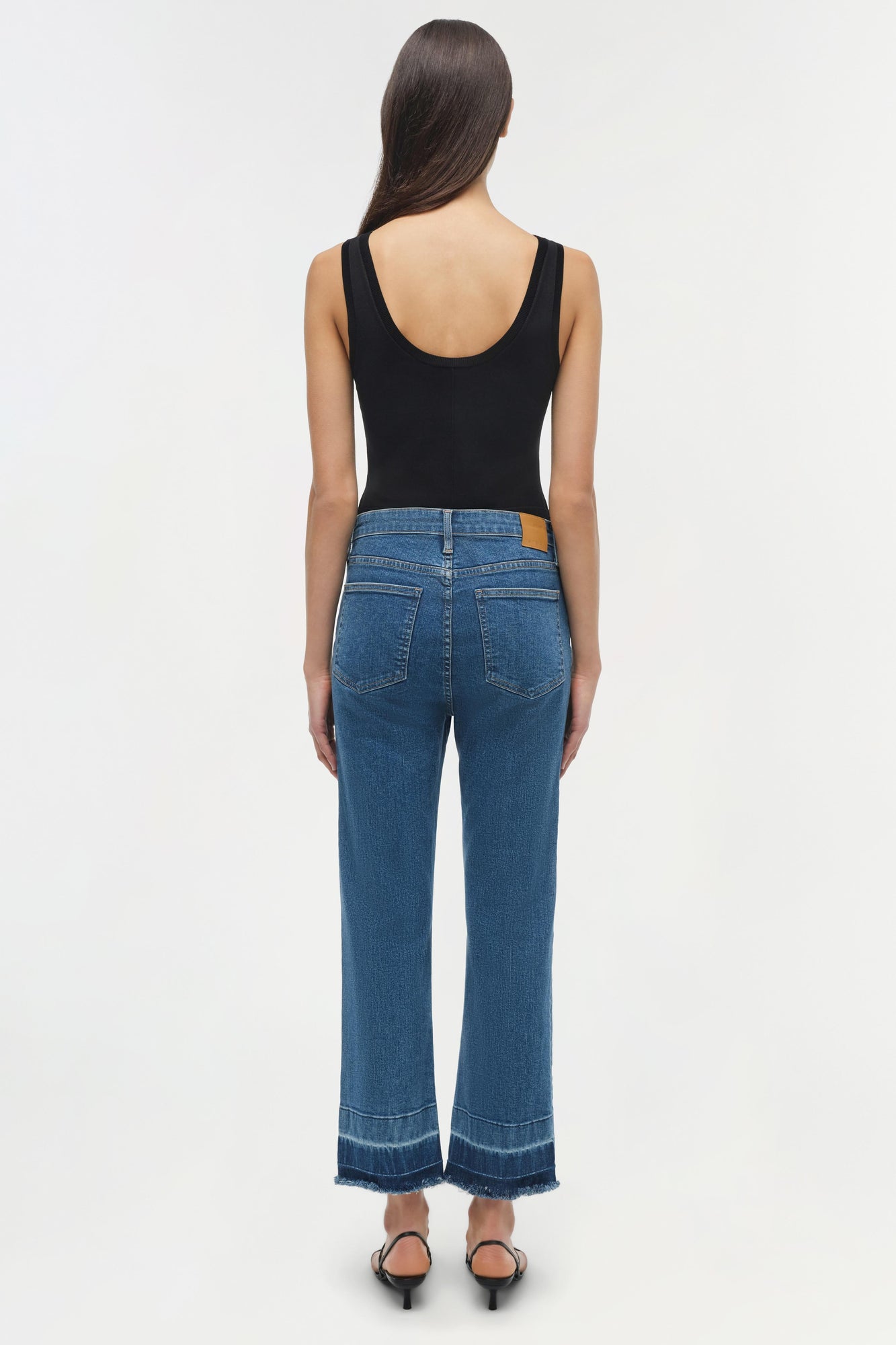Woman wearing blue straight-leg jeans with frayed hems and a black sleeveless top, viewed from behind.