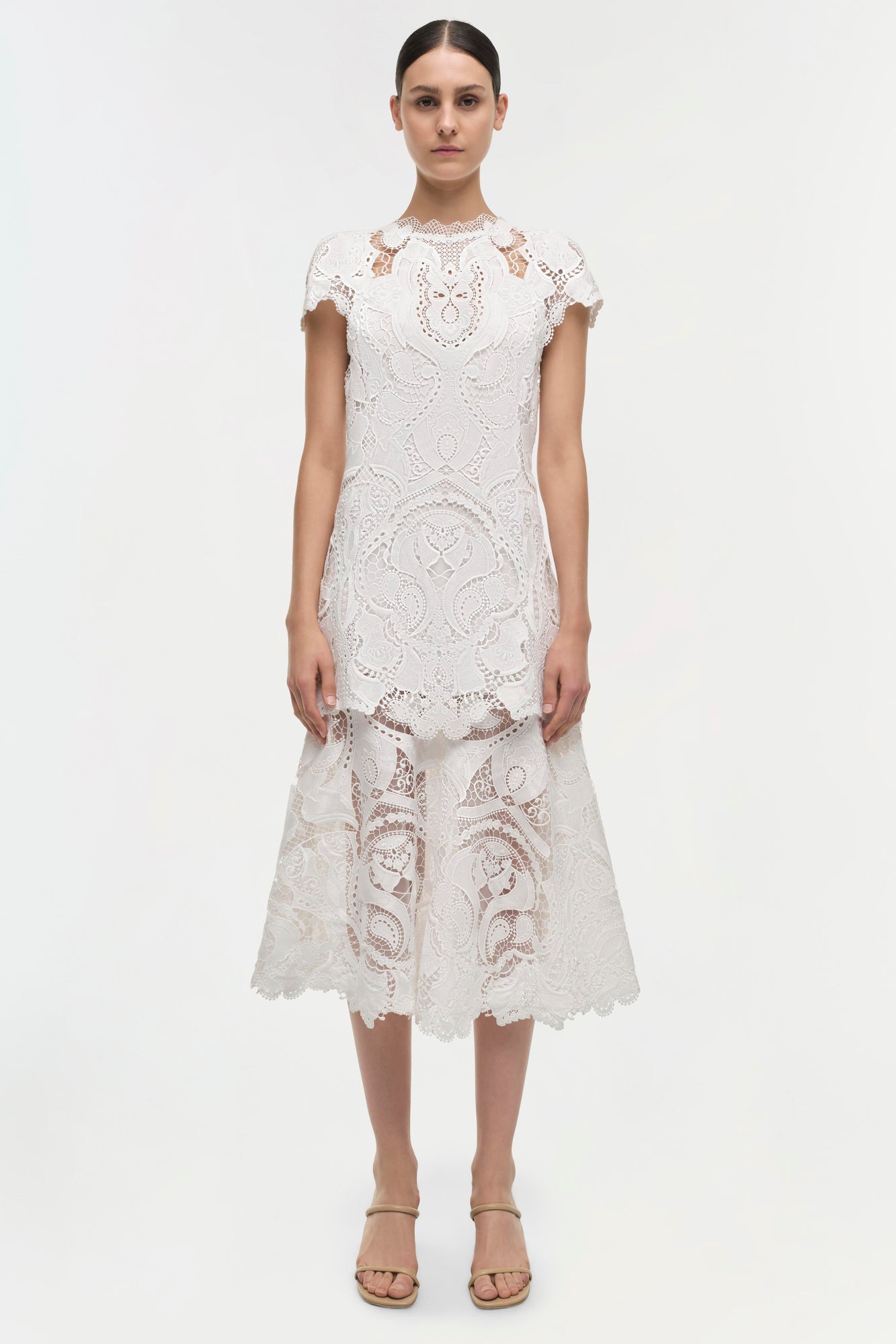White lace dress with short sleeves, crew neckline, and tiered midi skirt with cutout details.