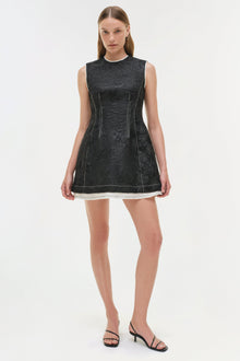 Black jacquard sleeveless mini dress with white trim at hem and vertical seam detailing, worn with black sandals.