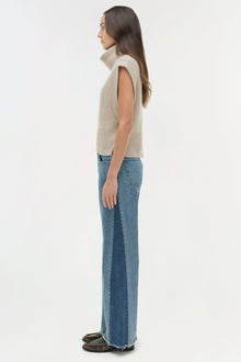 Woman wearing cream sleeveless turtleneck and blue straight leg jeans, side view.