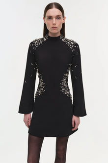 Black mini dress with crystal embellishments on shoulders, sides, and neckline; long flared sleeves.