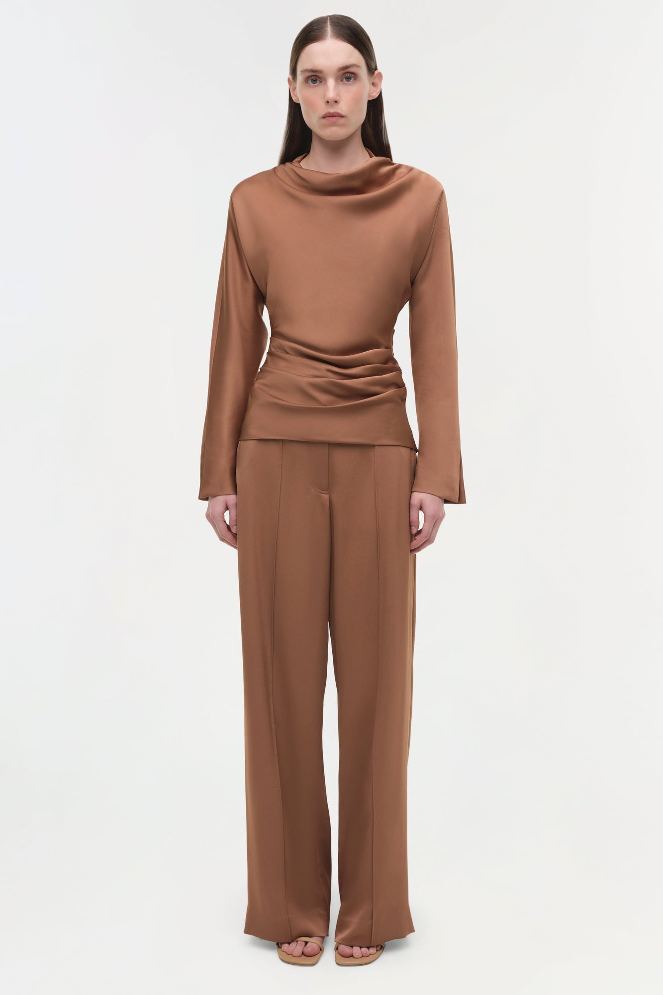 Camel satin long-sleeve top with cowl neckline and ruched side detail, worn with matching wide-leg pants.