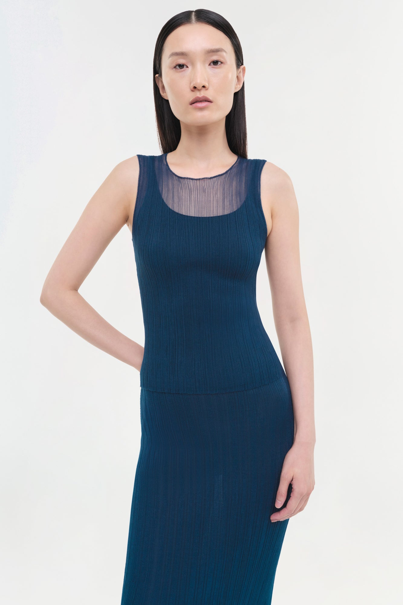 Dark teal ribbed tank top with sheer mesh panel at neckline worn by woman.