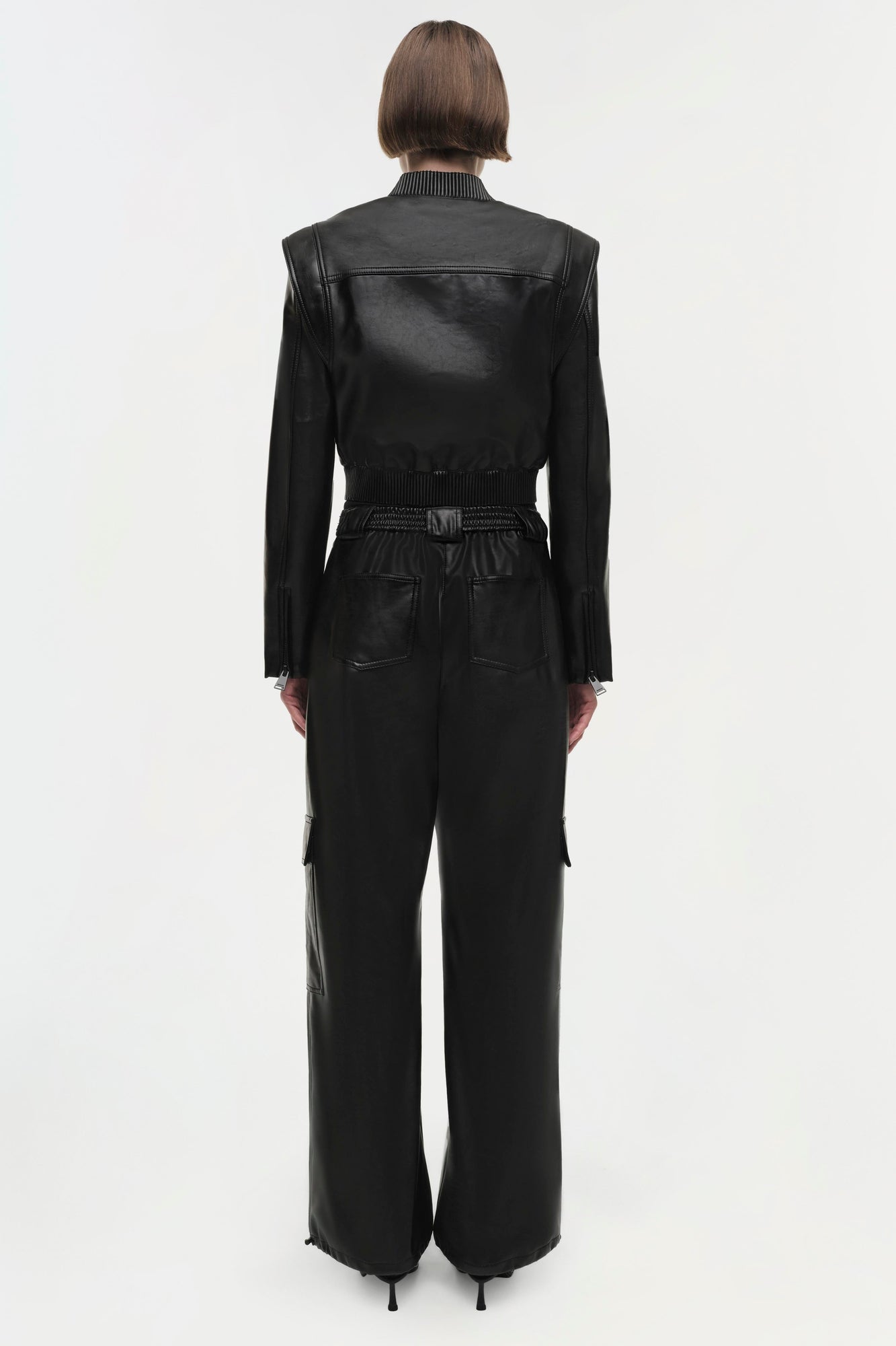 Black leather cropped jacket with ribbed collar and long sleeves, shown from back on model.