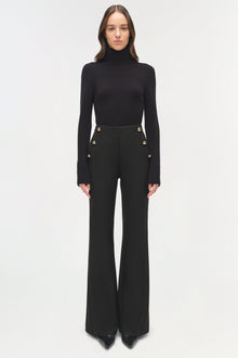 Black tailored trousers with decorative buttons at waist, paired with black turtleneck sweater.