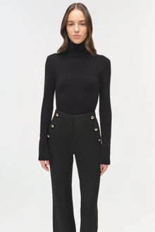 Black tailored trousers with gold button details at the waist, paired with a black turtleneck sweater.