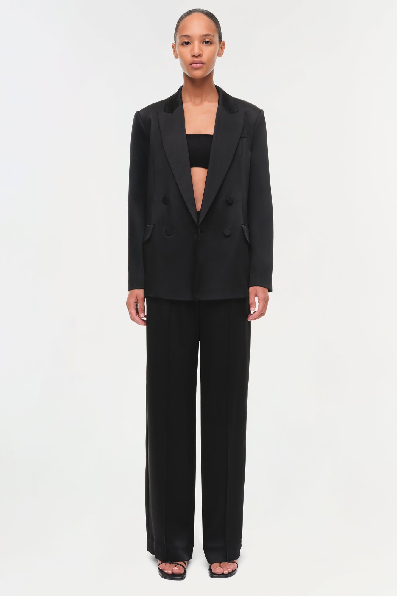 Black double-breasted satin blazer with peaked lapels worn open over matching pants.
