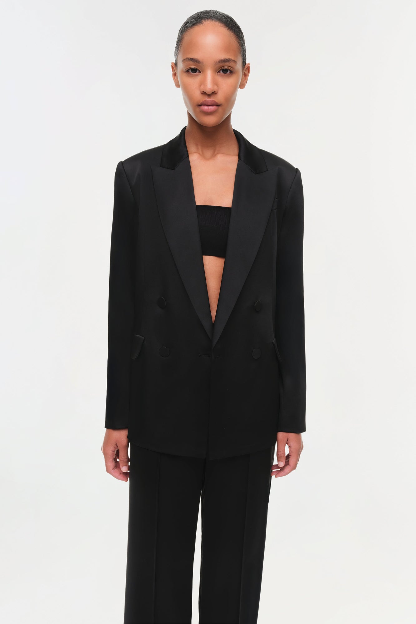 Black satin blazer with peaked lapels and double-breasted buttons, worn open over matching trousers.
