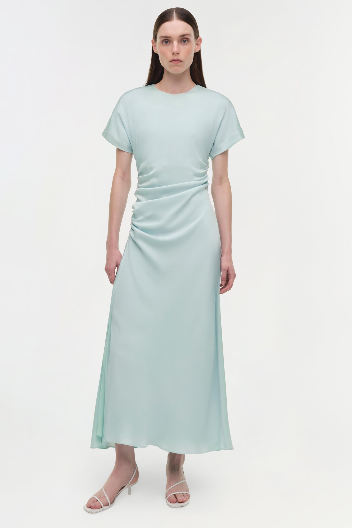 Light green satin midi dress with short sleeves and ruched detailing on the side, worn with white strappy sandals.