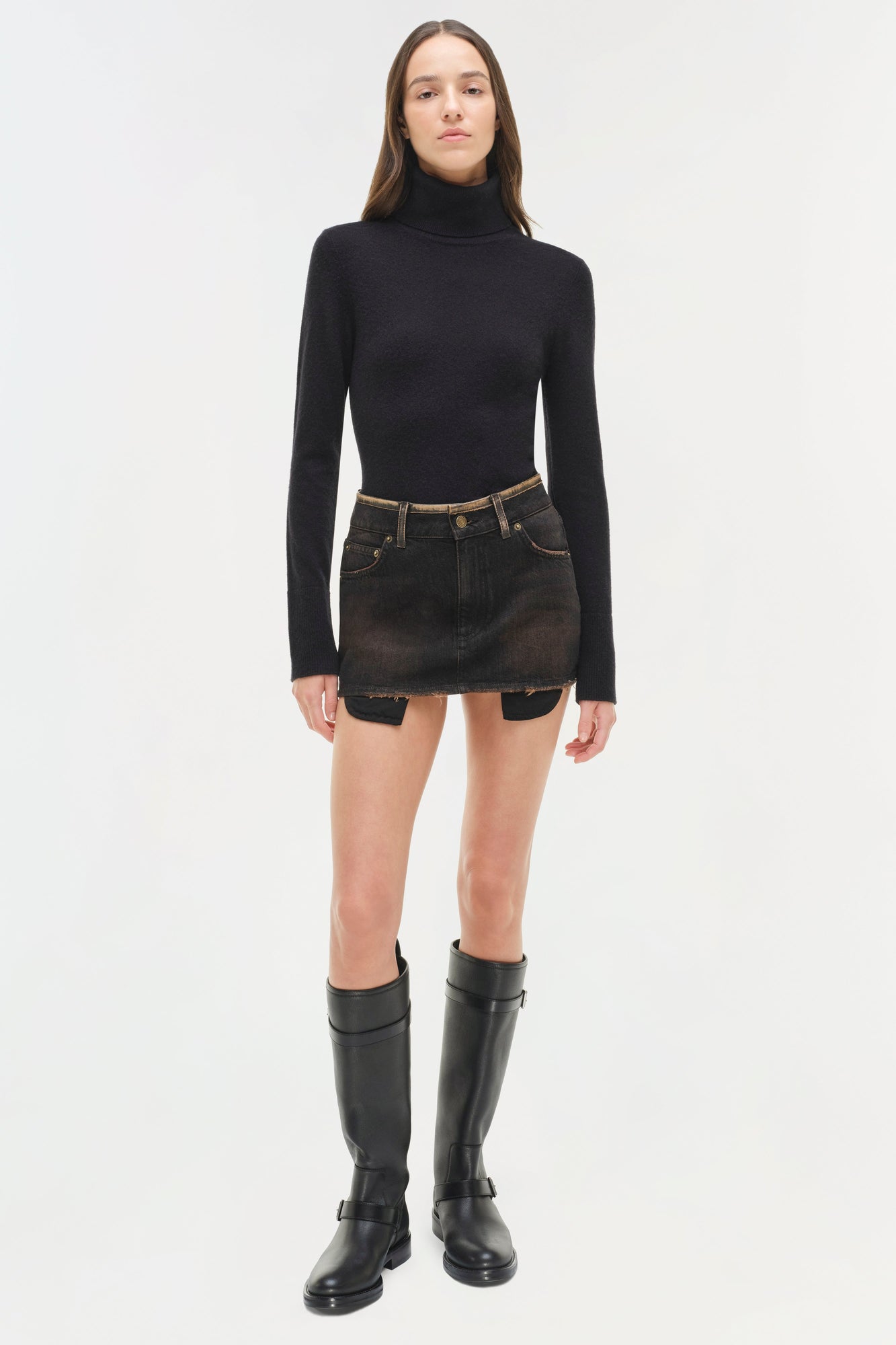 Black denim mini skirt with distressed hem and brown belt detail, styled with black turtleneck and boots.