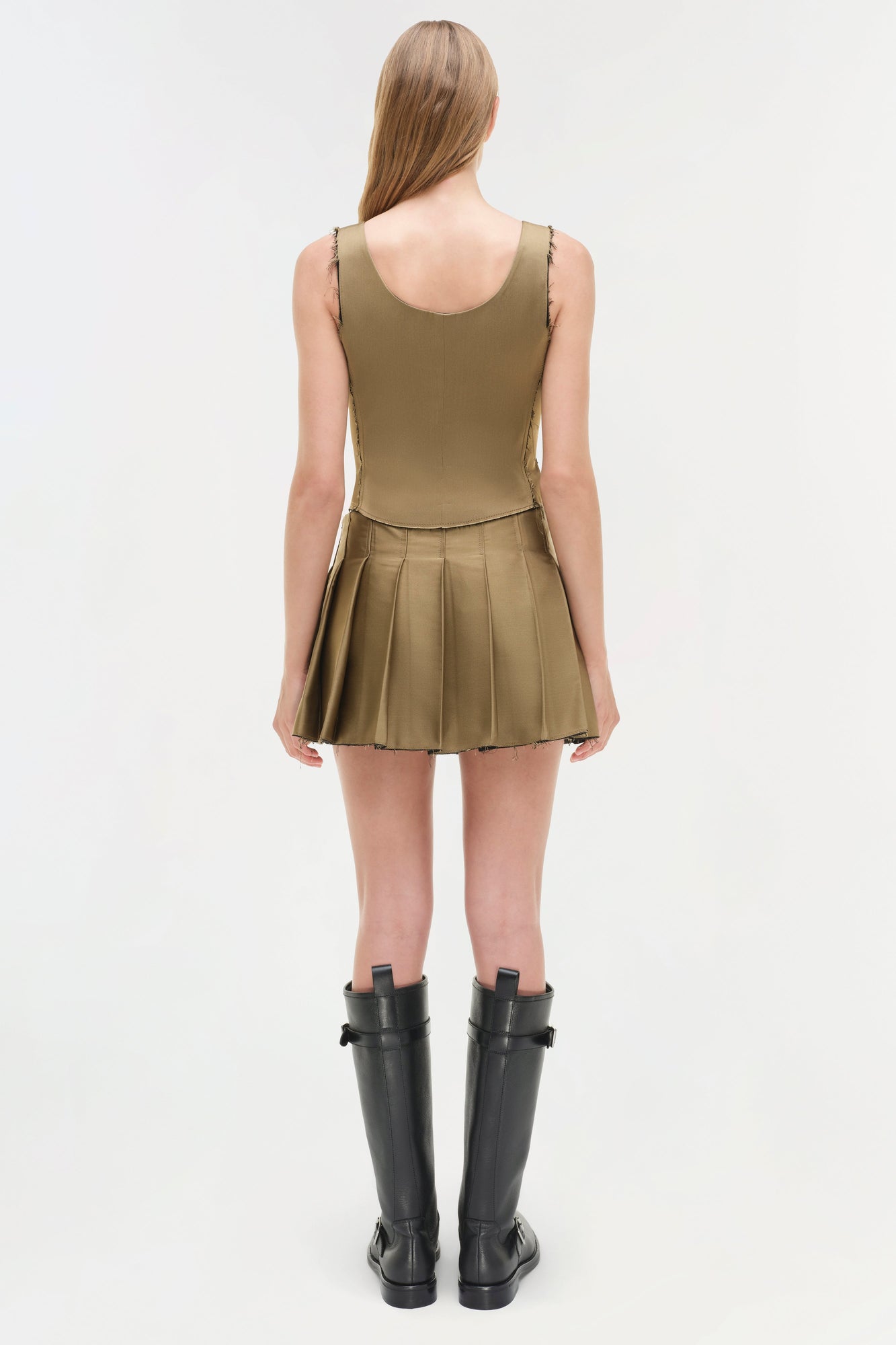 Olive pleated mini skort with sleeveless tank top, styled with black knee-high boots.