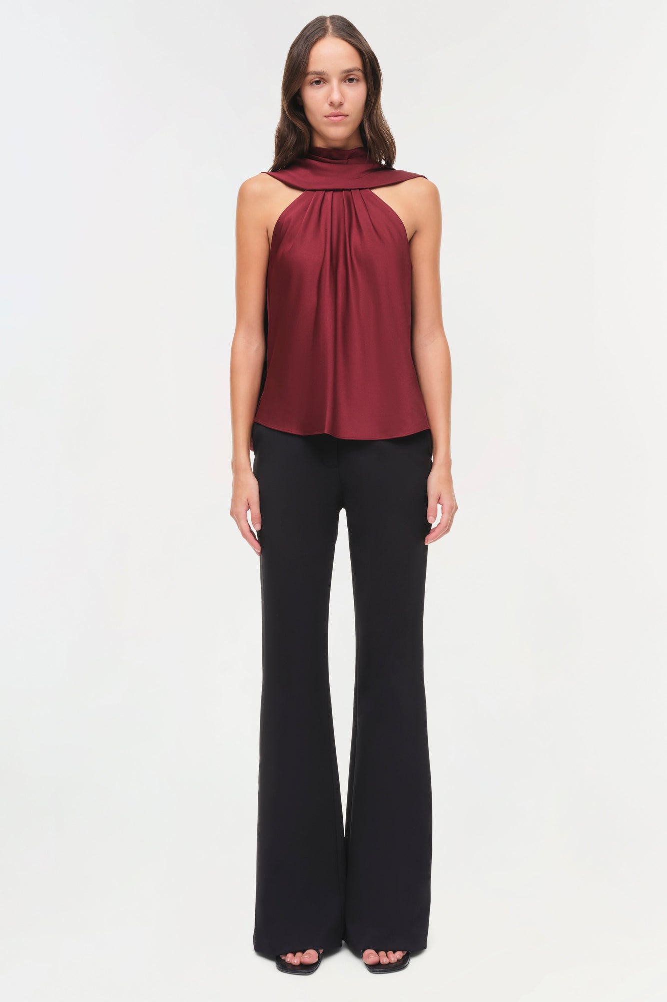 Burgundy satin halter top with draped cape collar and black flared pants.