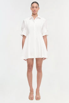 Woman wearing a white button-up shirt dress with rolled sleeves and a flared skirt, paired with beige sandals.