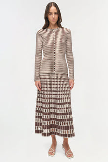 Woman wearing brown and cream striped knit cardigan with matching patterned midi skirt and white sandals.