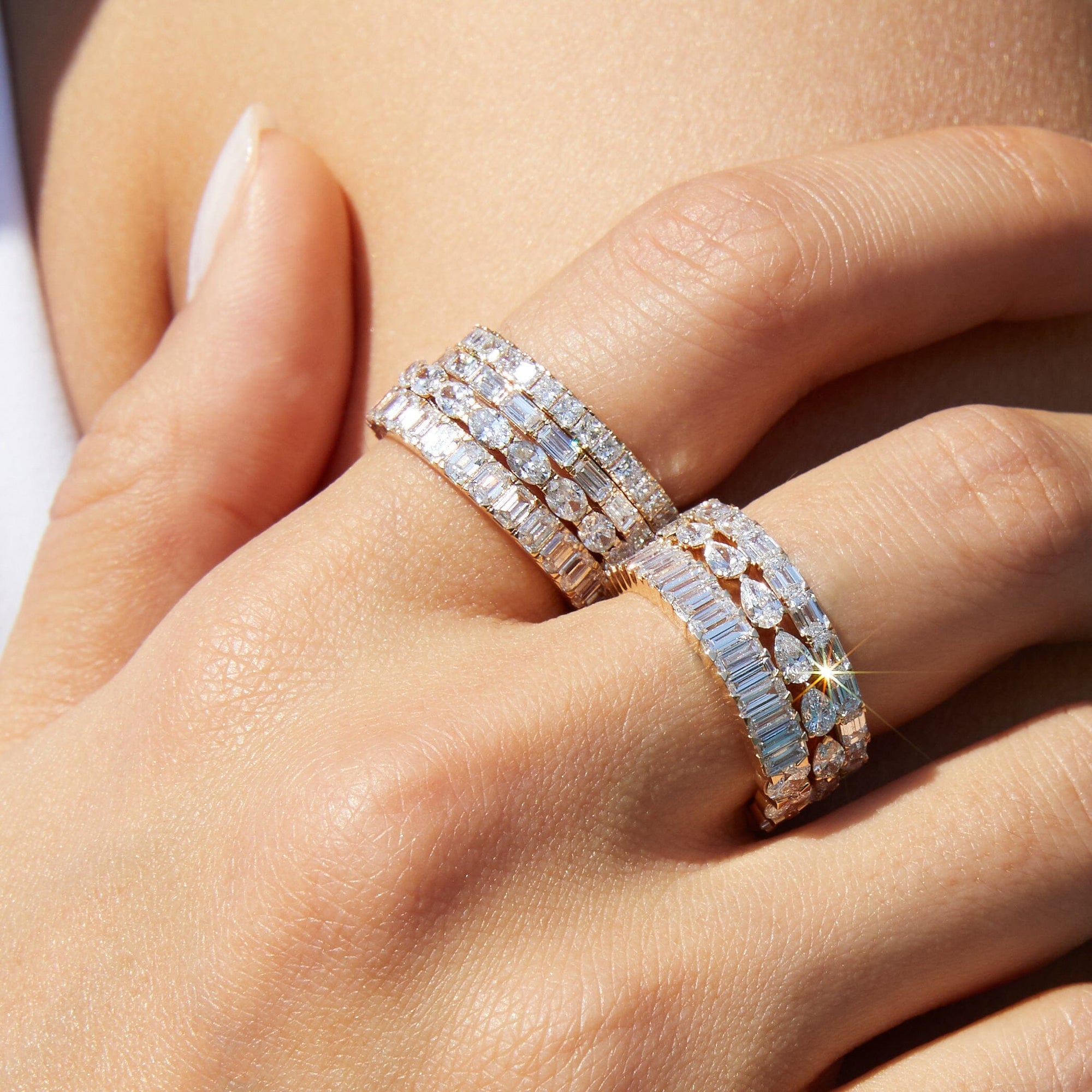 Lifestyle Model Close-up of a woman's hand resting against her skin, wearing multiple stacked gold and diamond eternity rings featuring mixed cuts, including pear and emerald shapes