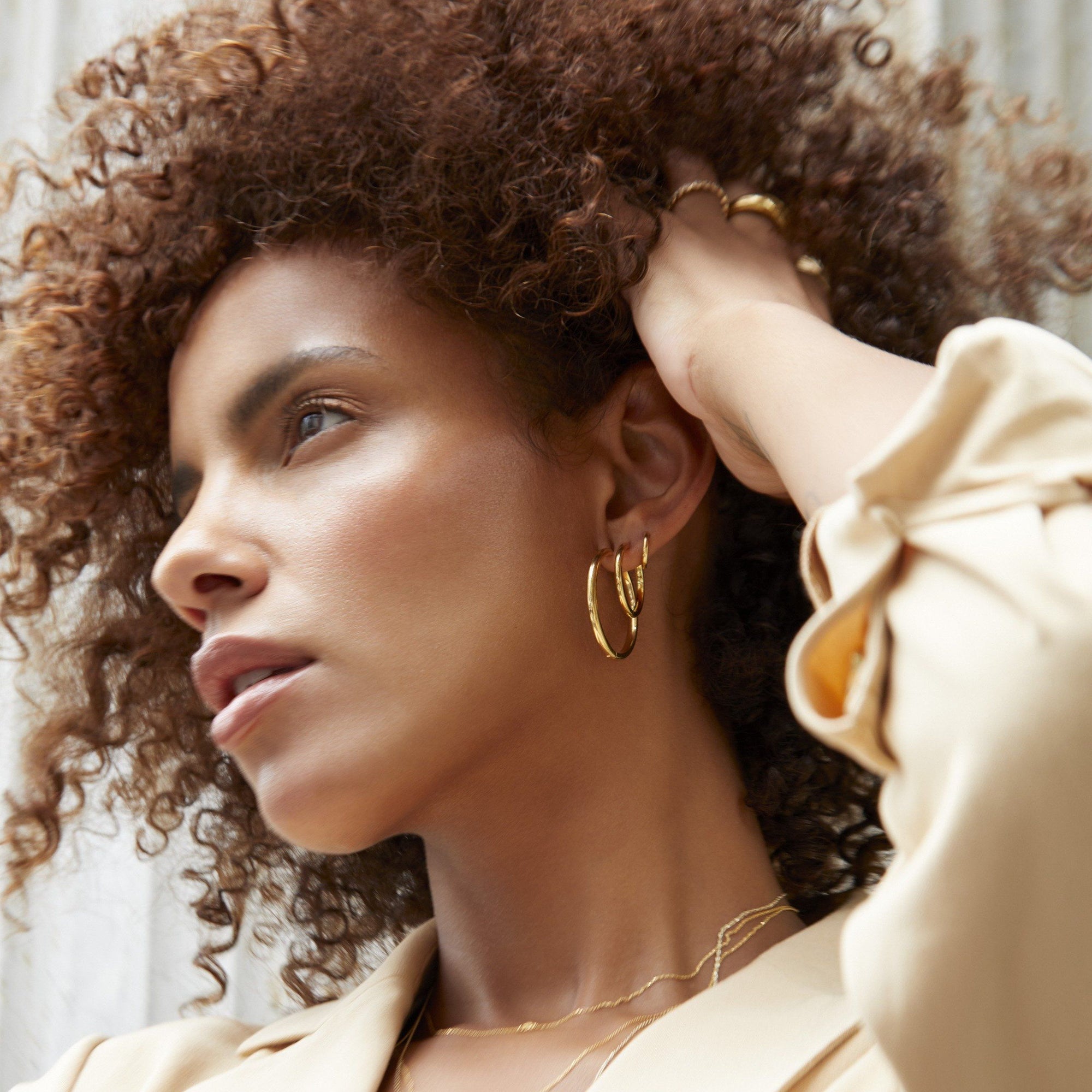 Model. Woman with curly hair wearing gold hoop earrings indoors