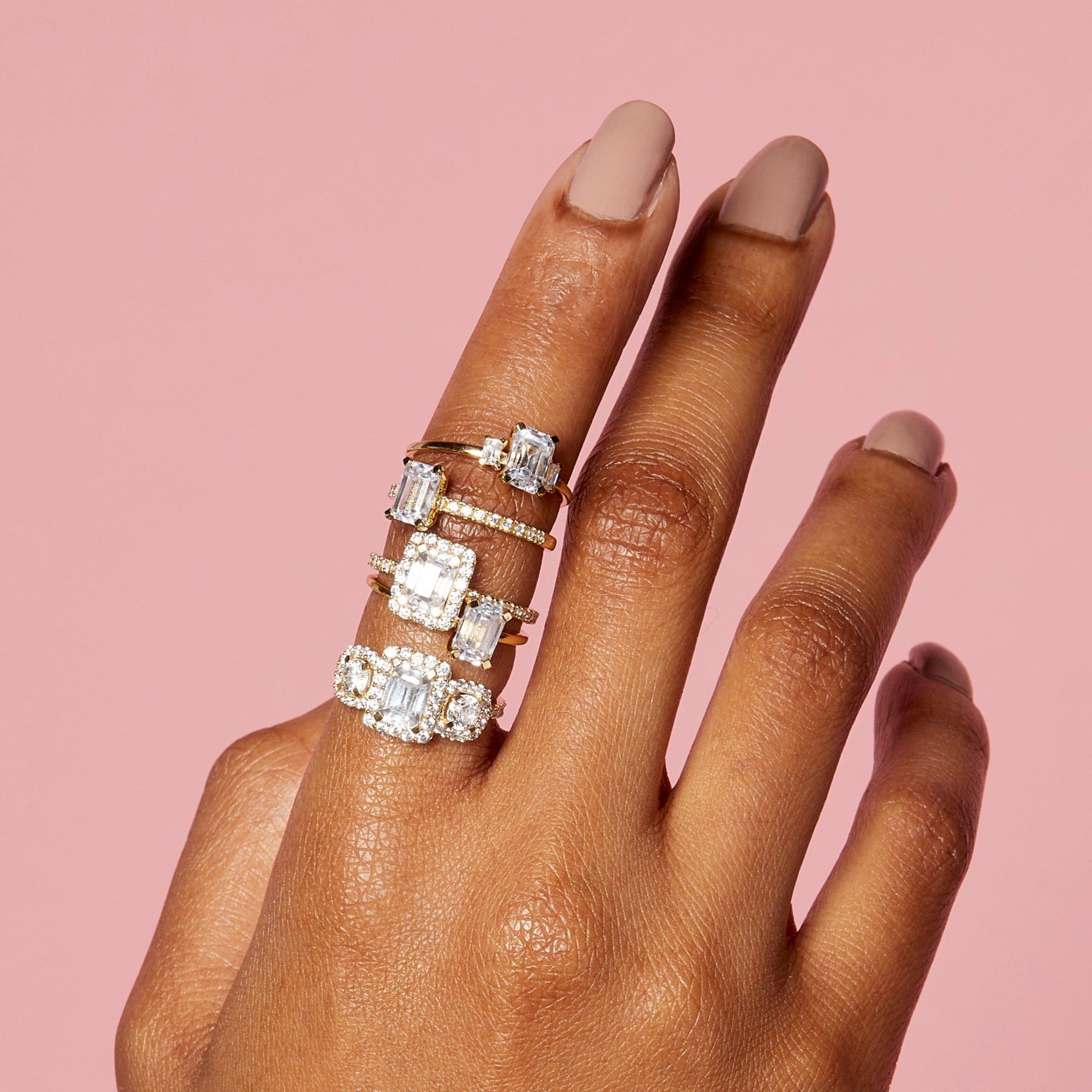 Lifestyle Model. Close up of hand with stakced engagement rings on pink background