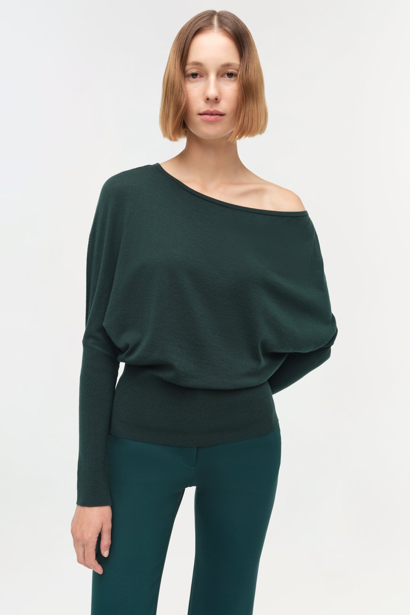 Dark green off-shoulder sweater with long sleeves and ribbed waistband worn with matching pants.