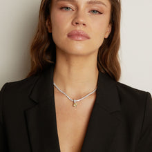 Model. Tennis necklace with a round gemstone pendant worn by a woman against a neutral background.