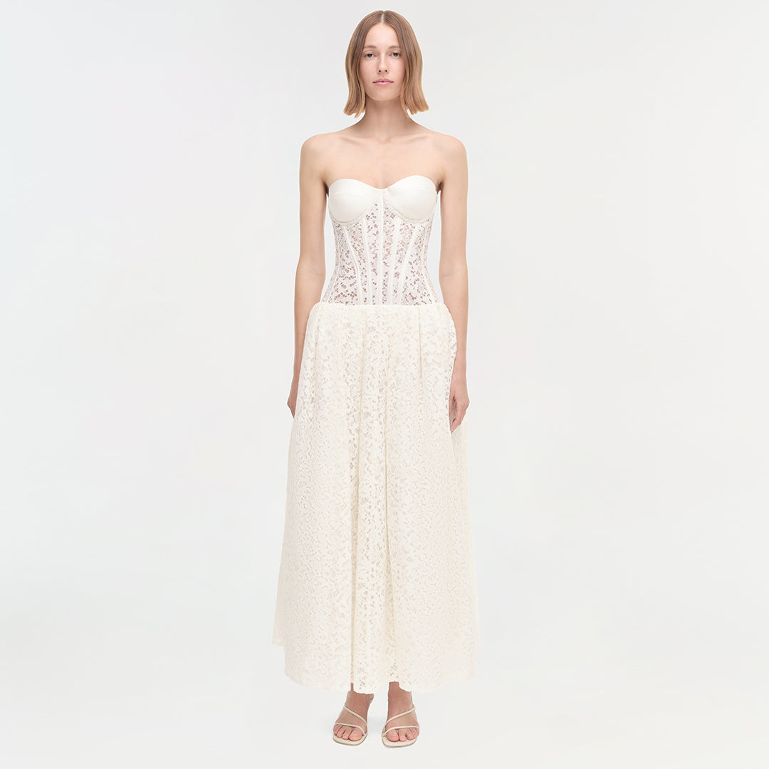 Woman wearing cream strapless dress with lace bodice and pleated skirt, paired with beige sandals.