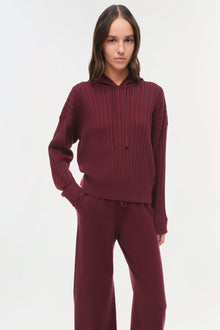 Woman wearing burgundy cable-knit hoodie and matching wide-leg pants against white background.