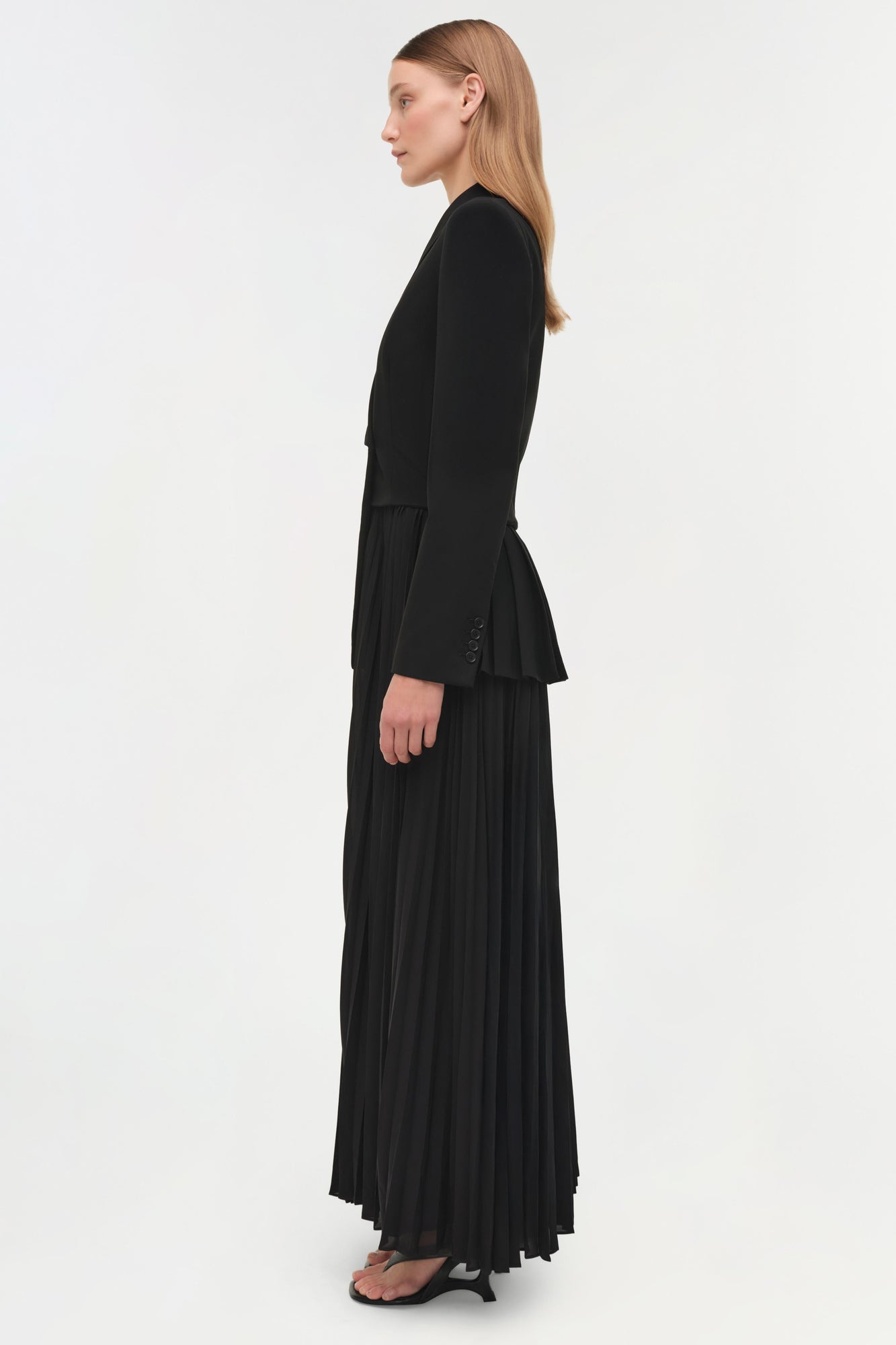 Black blazer midi dress with pleated skirt and button front, shown on model from side profile.