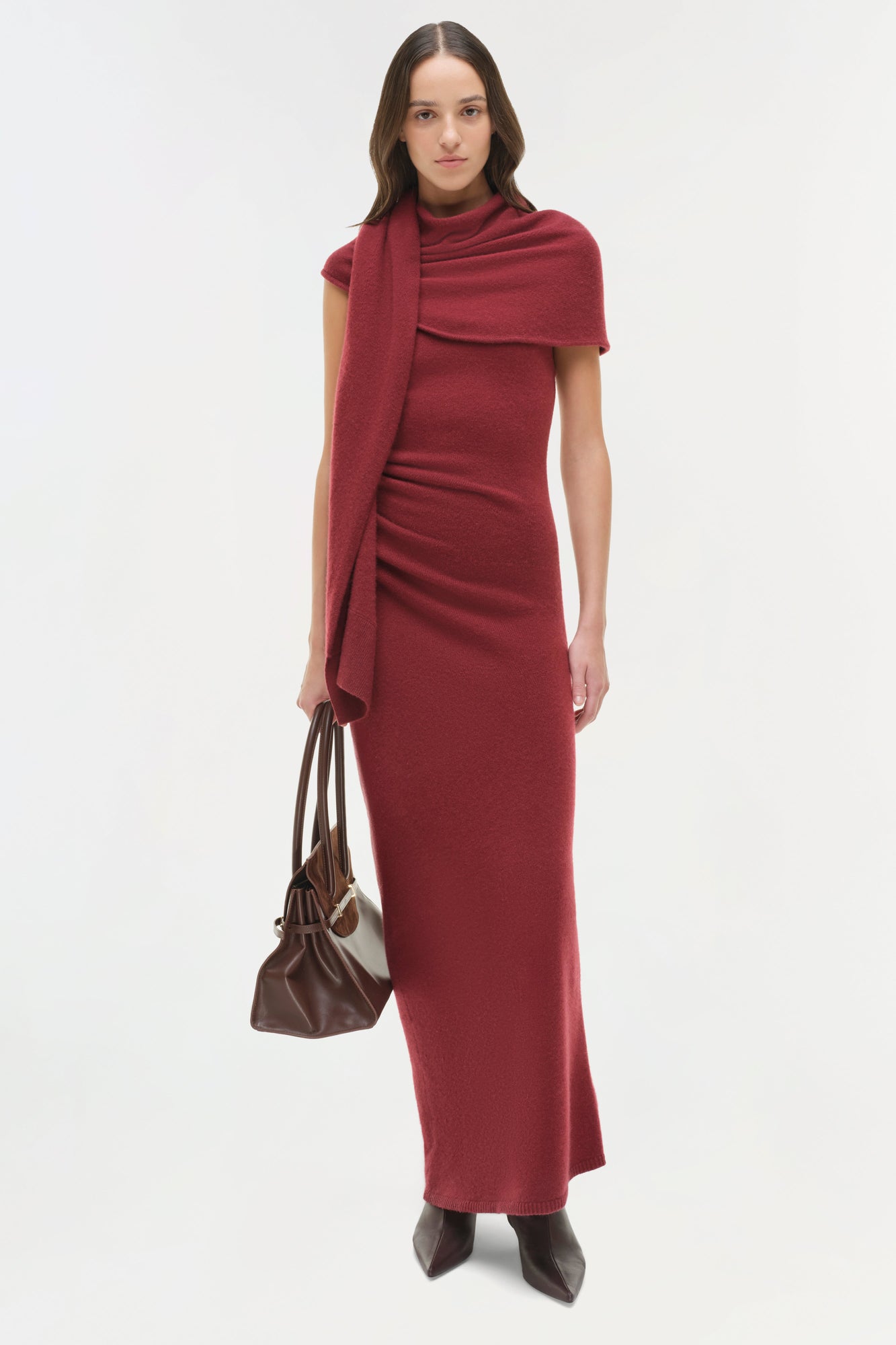 Burgundy midi dress with short sleeves, draped shoulder wrap, and matching scarf detail worn with brown leather handbag.