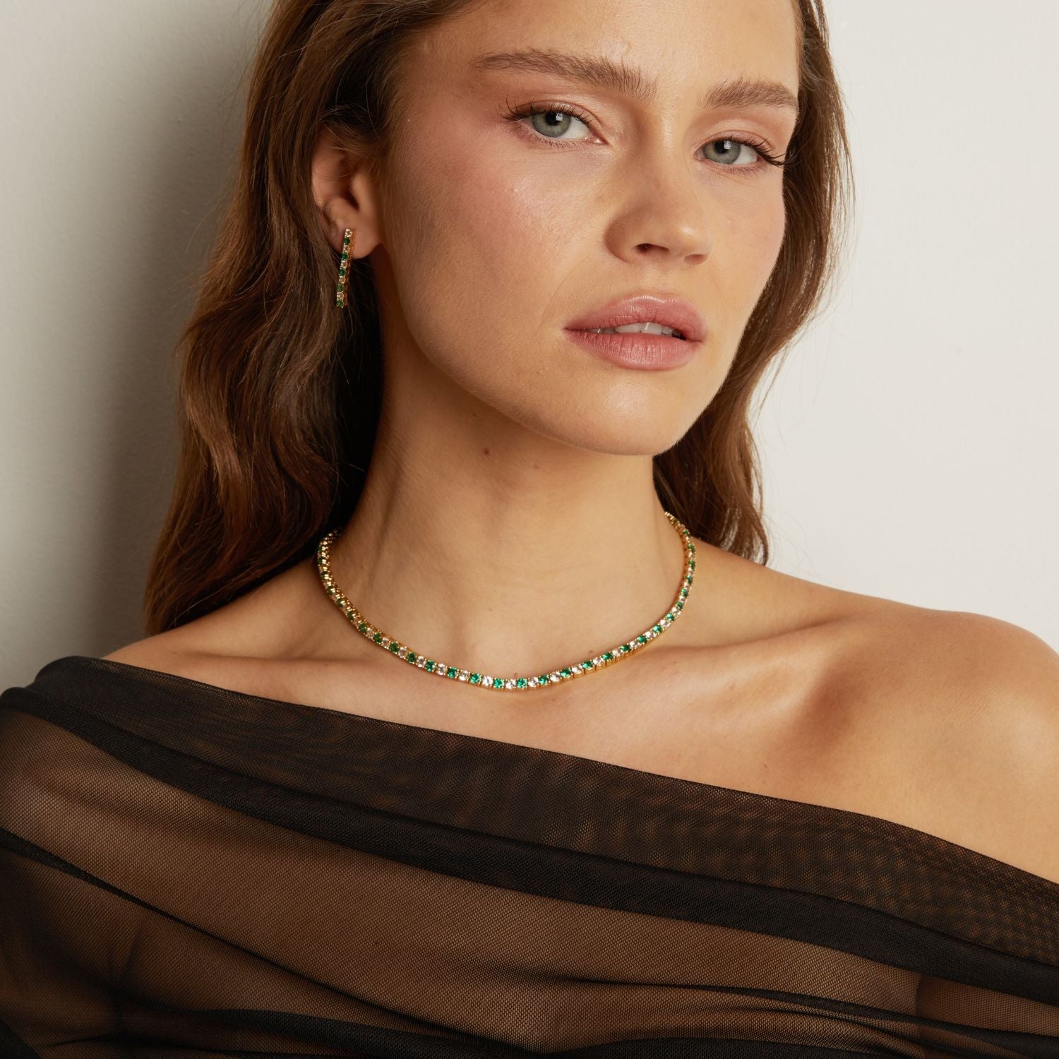 Model. Woman wearing a green and gold necklace against a neutral background