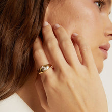 Close-up of a woman wearing a gold ring on her hand, with a neutral background.